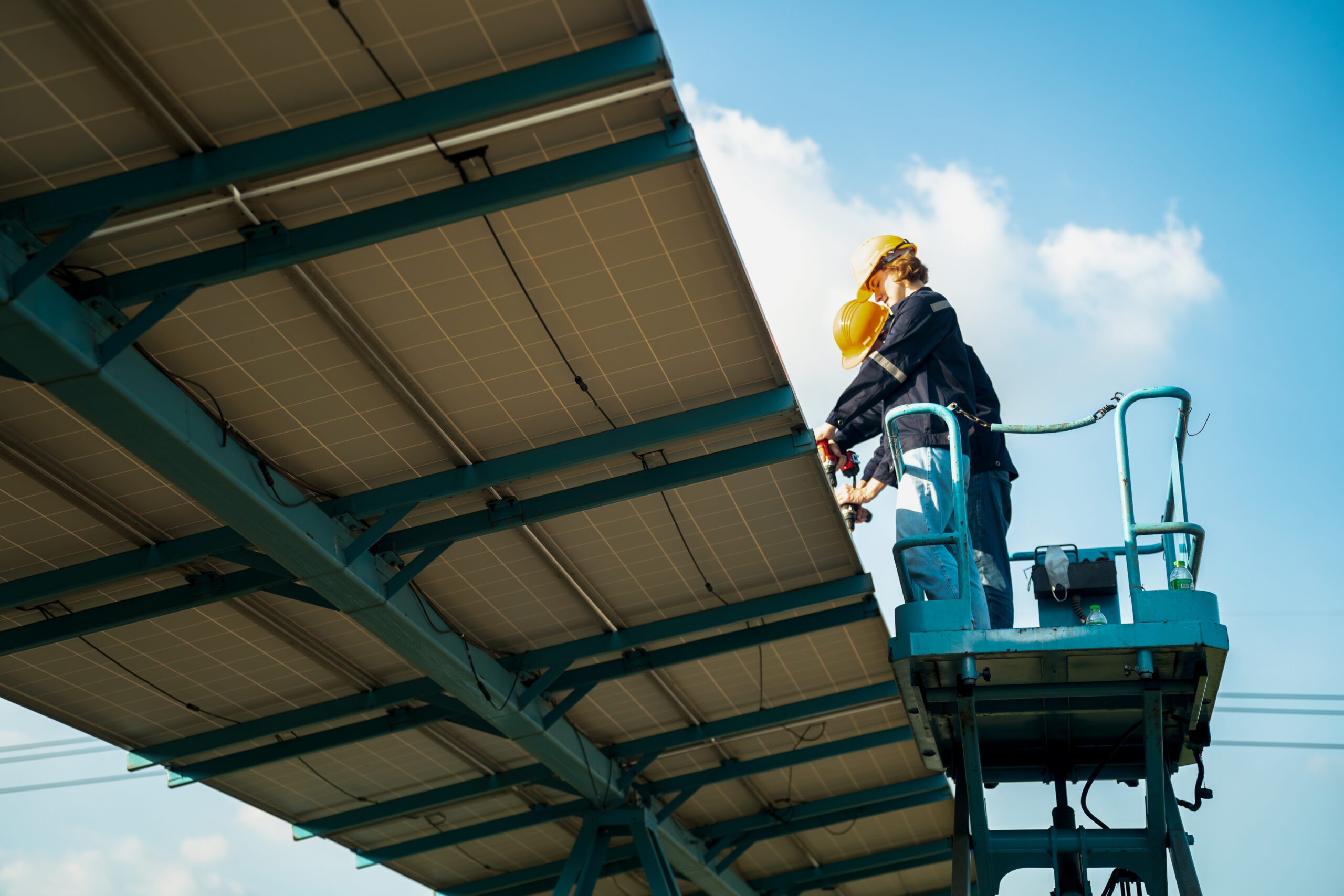 Homme sur une nacelle entrain d'installer des panneaux photovoltaïques sur une ombrière de parking